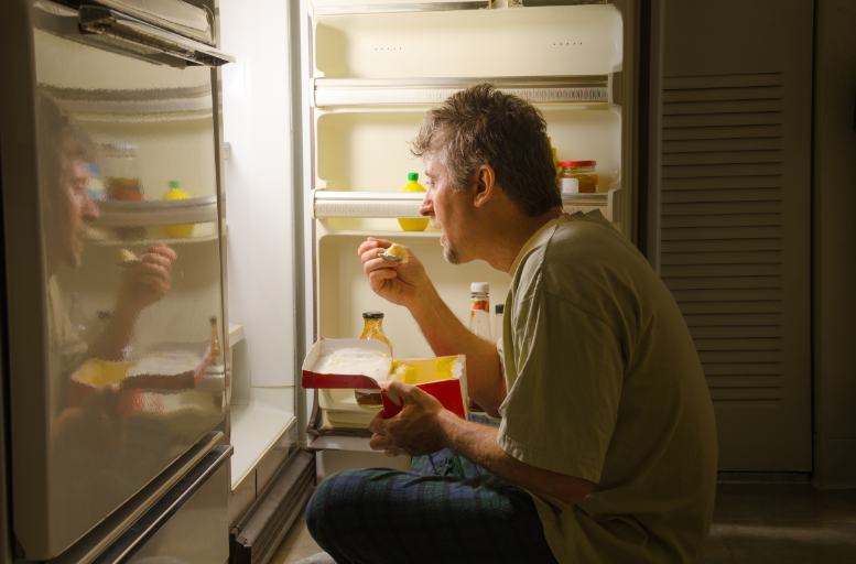 Man binge eating in front of the refrigerator