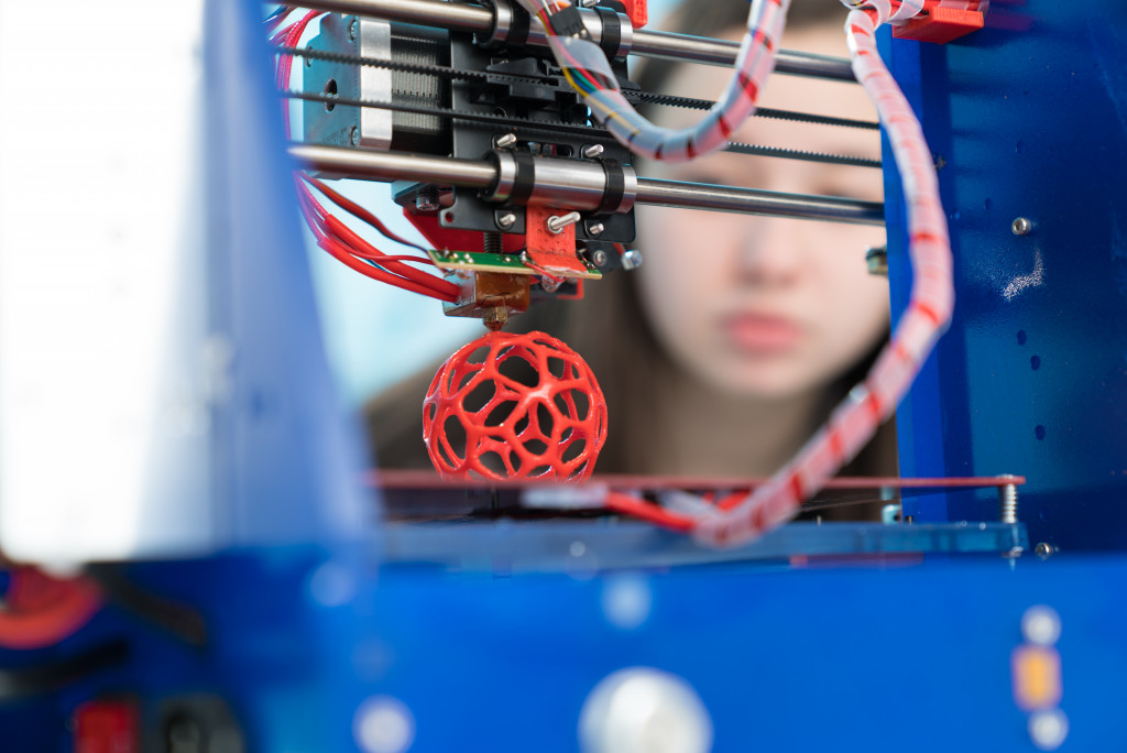 girl watching as a 3d printer is working its magic on a red filament