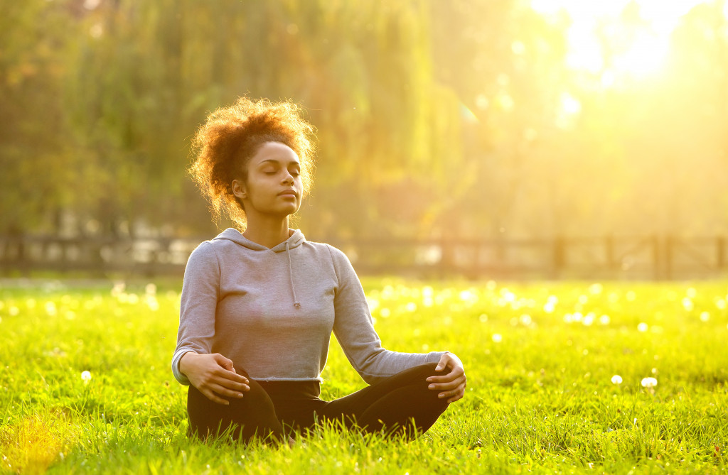 Woman sits cross legged outdoors on the grass while meditating