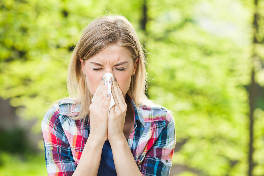 A woman sneezing outdoors due to allergies