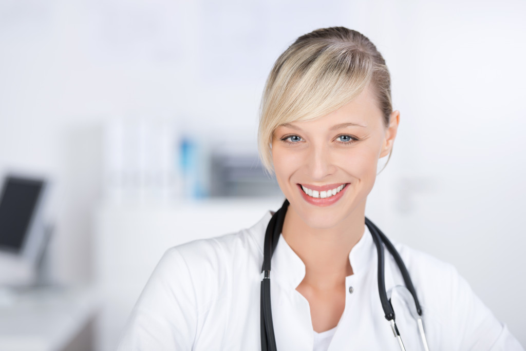 Smiling female doctor with a stethoscope and wearing a medical gown.